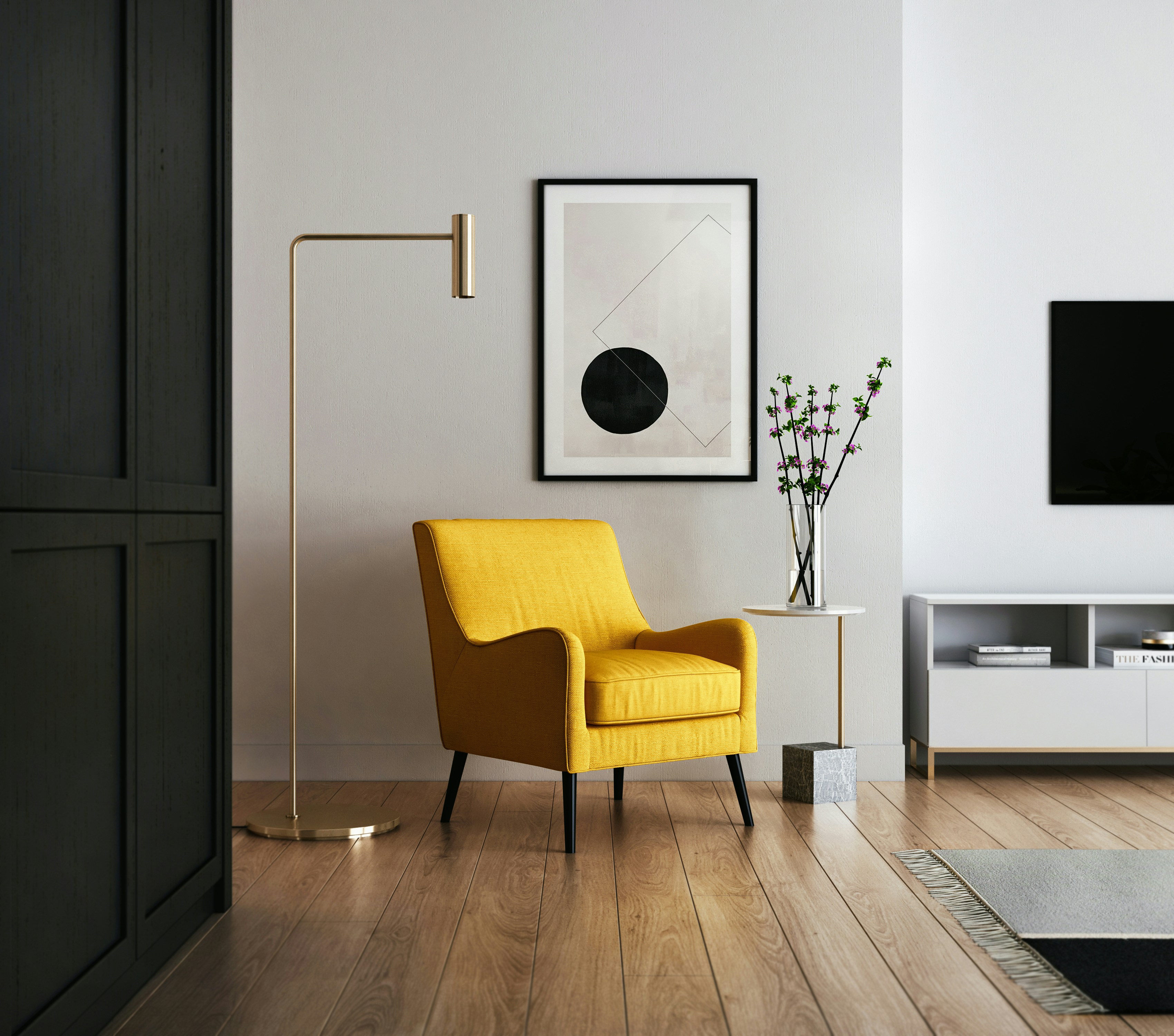 A minimalist living room with a mustard-yellow armchair next to a sleek, gold floor lamp and a small white side table. A framed abstract art piece hangs on the wall, with a vase of branches on the table. The room has light wood flooring and a modern aesthetic. Photo by Kam Idris.