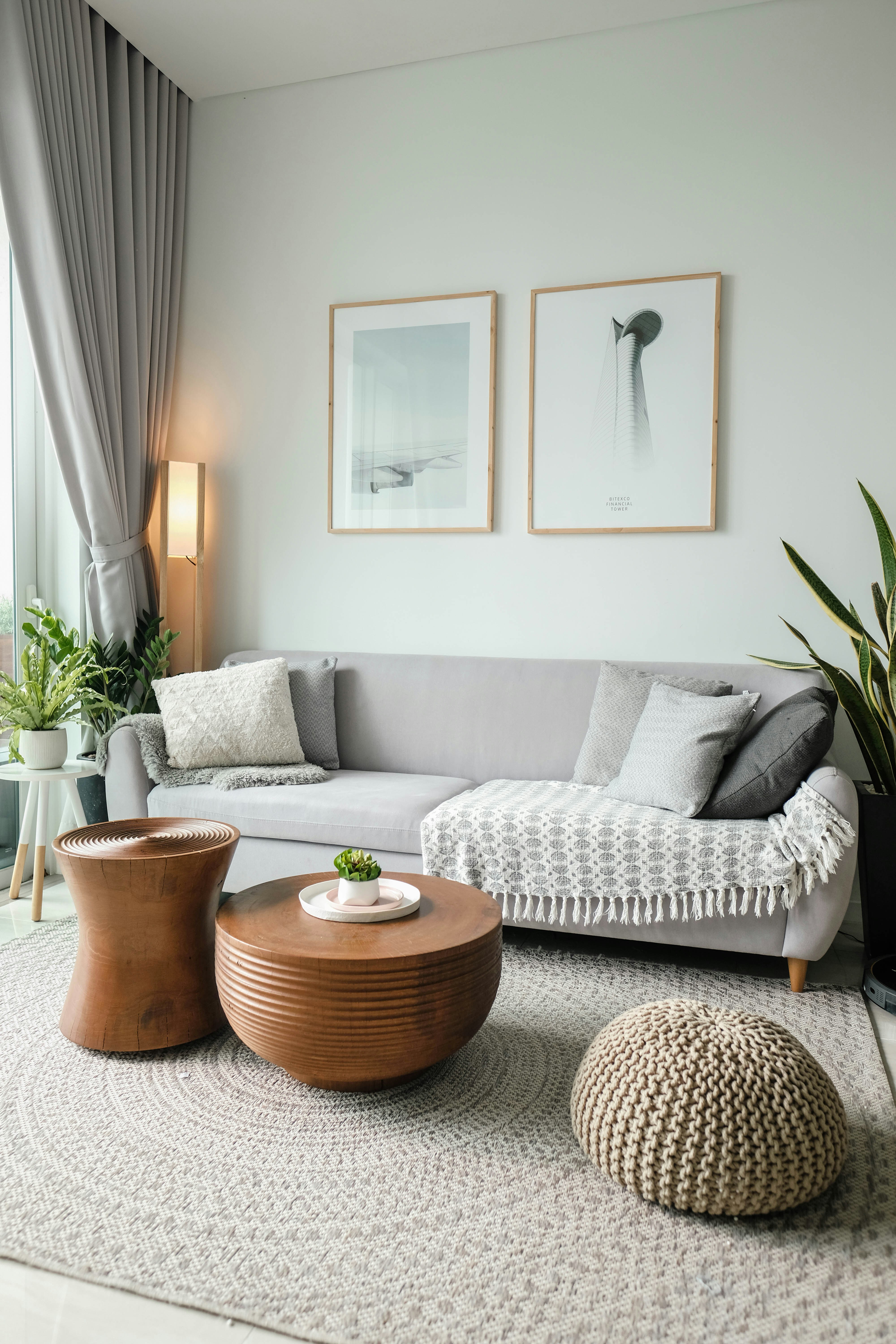 A young woman with red hair sits on a gray sofa, smiling as she holds a book with her Shiba Inu dog resting beside her, looking at the book. The room features modern decor, with shelves and plants in the background. Photo by Vitaly Gariev.